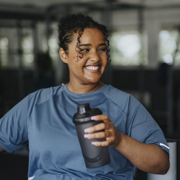 Happy young woman with water bottle taking break at gym