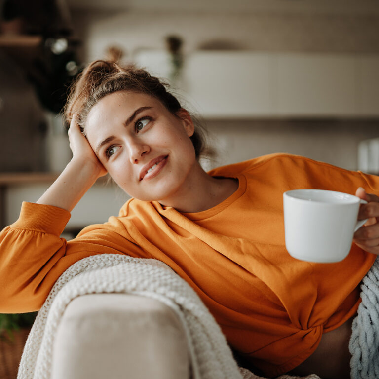 Young woman resting on sofa with cup of tea.